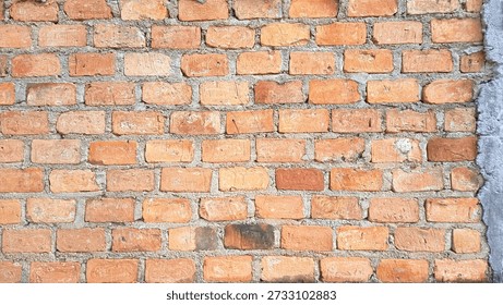 Old red brick wall texture with visible cement mortar in natural daylight. Rustic brick pattern background showing rough surface details, weathered tones, and traditional construction style. Ideal for architectural design, urban background, industrial themes, renovation concepts, and textured wallpaper use.