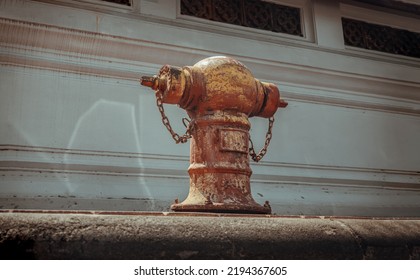 A Old red fire hydrant on sidewalk in Front of an on white cement wall for fire fighting on land, the water is pumped through the hydrant to a tank on a fire. Copy space, Selective focus.