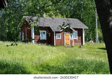 Old red logcabin in Finland. Red cabin next to forest and meadow in summer.