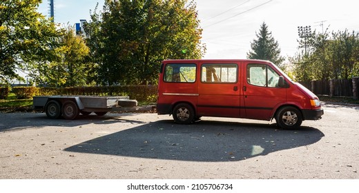 old red minivan in tow with open empty metal trailer standing on asphalt road of city street - Powered by Shutterstock