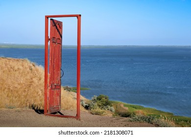 An old red open door stands on a cliff near the blue sea