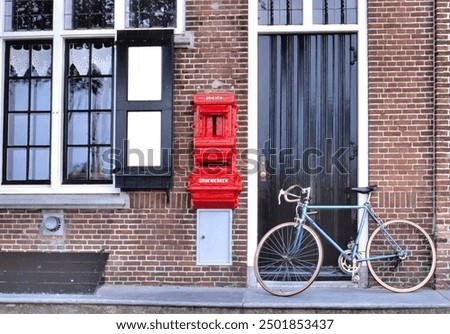 Old red postbox mounted in a brick wall of a house with the text BRIEVEN (letters) and DRUKWERKEN (press-work or printed matter) with next to it an old fashioned bicycle 