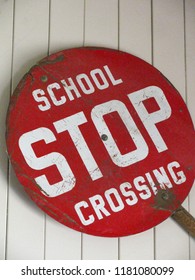 Old, Red School Crossing Stop Sign, With Large White Lettering And Handle For Crosswalk Guard To Hold. Isolated On White Wood Background.