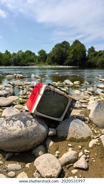 Old red Television abandoned on a river stone\
out of date and without\
emission