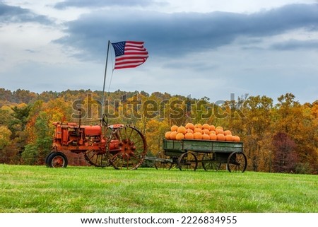 An old red tractor with a American Flag, sits in a field hitched to a wagon full of pumpkins in rural Virgina.
