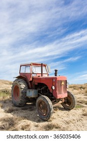 Old red tractor in the field with a cloudy sky