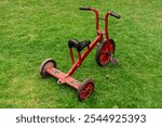 Old red tricycle with a worn look standing on green grass, evoking memories of outdoor childhood play