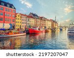 An old red and white fishing boat stands among other ships and yachts near the old small multi-colored houses in the Nyhavn canal. Copenhagen, Denmark
