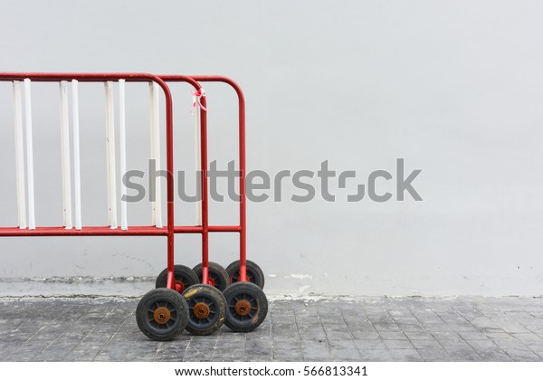 old red and\
white road security steel barrier on wheel, on grey cement wall\
background and pathway, copy space\

