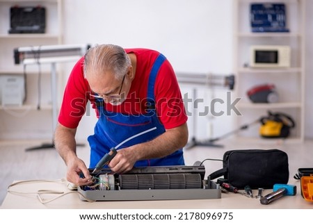 Old repairman repairing air-conditioner at workshop