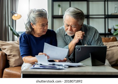 altes pensioniertes asiatisches Ehepaar, das die Finanzabrechnung gemeinsam auf dem Sofa überprüft und berechnet, das Finanzpapiere bearbeitet, Steuern zahlt, die online über einen E-Banking-Laptop auf Wohnzimmerhintergrund bezahlt werden