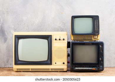 Old Retro Analog Small TV Sets Stand On Wooden Floor Front Grey Concrete Wall Background.