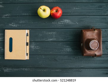 Old retro camera and blank notebook and apple on the gray wooden background