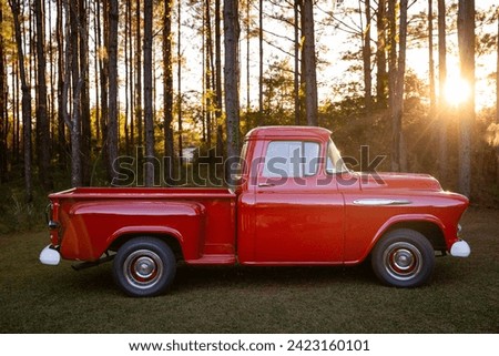 An old retro classic vintage red American pickup truck parked outside in the country with hazy light flare at sunset.