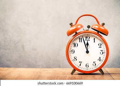 Old retro orange alarm clock on wooden desk front concrete wall background. Vintage style filtered photo