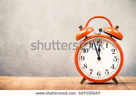Old retro orange alarm clock on wooden desk front concrete wall background. Vintage style filtered photo
