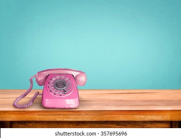 Old retro pink telephone on table with vintage green pastel background