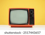 Old retro red TV on white table with blank screen on yellow background, front view.