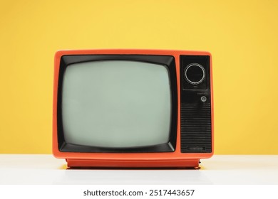 Old retro red TV on white table with blank screen on yellow background, front view.