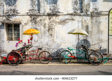 An old rickety trishaw cab parked on the sidewalk of a dilapidated building in Penang, Malaysia. - Powered by Shutterstock