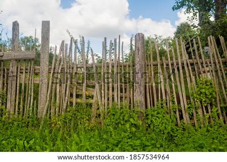 Old rickety wooden fence made of narrow boards in front of village house.