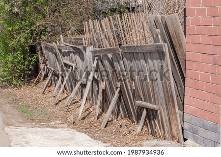 Old rickety wooden fence with props. Brick wall nearby. Green bushes on the background. Horizontal.