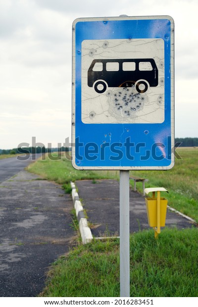 Old road blue bus stop sign damaged by pistole\
bullets by asphalt road