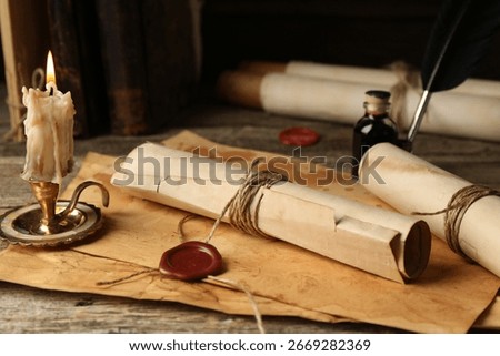 Old rolled paper scrolls, sheets and burning candle on wooden table, closeup