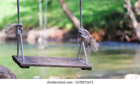 Old Rope Empty Wooden Swing Near Riverside Nature Park Outdoor , Summer Vacation Holiday.