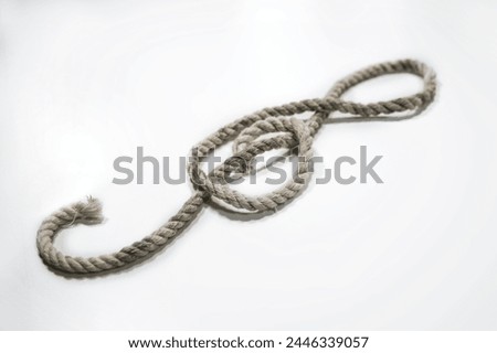 Old rough rope laying in the shape of a treble clef or violin key on a light gray background, musical symbol, copy space, selected focus, narrow depth of field