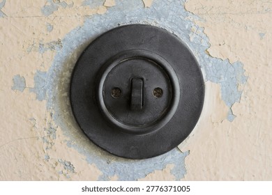 Old round Bakelite light switch on a wall with weathered paint