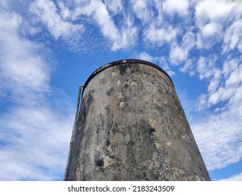 An Old Round Water Tank Soaring Into The Sky. Made Of Large Cement In The Outdoors. There Are Various Black Stains Caused By Rain And Sunlight, Causing The Condition To Change.