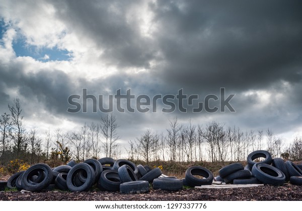 Old rubber tires dumped and polluting nature,\
dark cloudy sky background