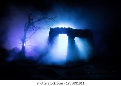 Old ruined stone house in deserted garden at night. Abandoned old mystic building with dead tree and misty backlight. Selective focus