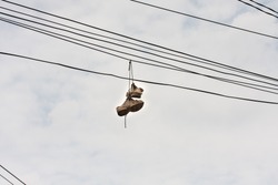 Old Running Shoes Hanging Outside In Electric Cables