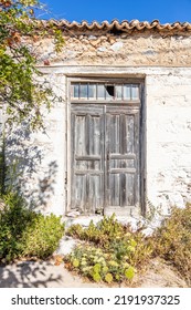 Old Rural Building Wall Facade, Ceramic Tiles On Rooftop, Wooden Aged Closed Door With Broken Glass On Top. Abandoned House, Dry And Green Plants Outdoors. Vertical