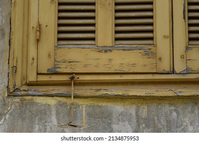 Old Rural House Window With Weathered Ochre Wooden Shutters And A Rusty Metal Latch In Nafplio, Greece.