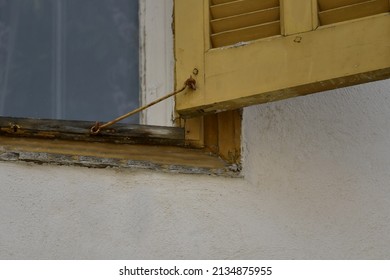 Old Rural House Window With Weathered Ochre Wooden Shutters And A Rusty Metal Latch In Nafplio, Greece.