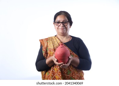 Old Rural Indian Woman Saving Money Holding A Piggy Bank And Wearing A Saree Portraying Various Expressions Of The Widow Life. She Is Confident And Portraying Savings Concept.