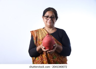 Old Rural Indian Woman Saving Money Holding A Piggy Bank And Wearing A Saree Portraying Various Expressions Of The Widow Life. She Is Confident And Portraying Savings Concept.