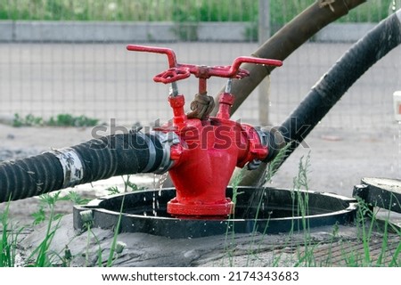 An old Russian red fire hydrant with two fire hoses pumps water from an open manhole. The concept of fire extinguishing.