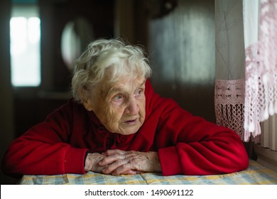 An old russian woman sits in a house near the window. 