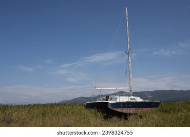 Old rusted abandoned yacht on the filed with a high grass. Mountains in the background. Blue sky with light white clouds in the spring. Roda, Corfu, Greece.