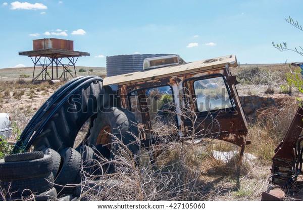 Old rusted car chassis with junk pile\
including tires with water tank in the background on old\
farmland/Abandoned Junk Pile/Western Australia\
Farmland