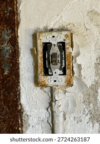 Old rusted light switch set into a cracked and peeling wall, showing signs of age, wear, and decay.

