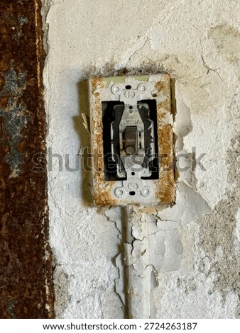 Old rusted light switch set into a cracked and peeling wall, showing signs of age, wear, and decay.
