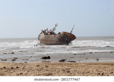 Old rusted shipwreck stranded on a sandy beach with ocean waves crashing against the shoreline.