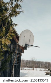 An old rustic basketball hoop with no net against a worn barn. In the background you can see open fields and freshly fallen snow.