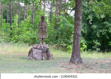 Old rustic statue of a peasant standing on the rock next to a tree in the middle of a dense forest bringing polish folk culture and beliefs to mind during a summer hot day