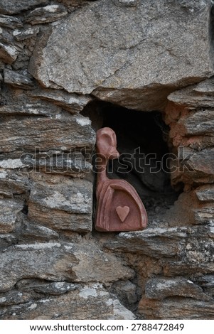 Old rustic stone wall with an arched niche and a small artistic sculpture in a historic village setting.